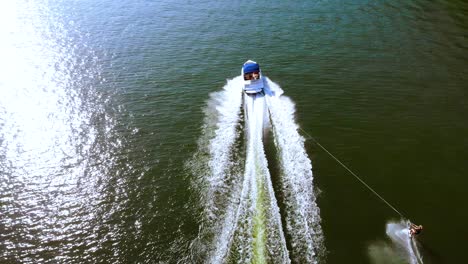 aerial drone footage of tourist enjoying water skiing, tied behind high speed motor boat