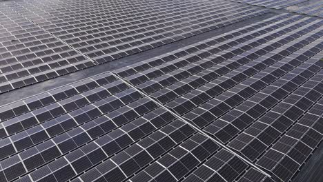 drone aerial footage flying above multiple rows of shiny solar panels in a power farm