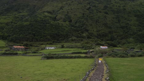 Mujer-China-Malaya-Asiática,-Con-Falda-Blanca-Y-Chaqueta-Amarilla-Corriendo-En-Un-Camino-Rural-En-Un-Pueblo,-Campos-De-Cultivo,-Isla-De-São-Jorge,-Las-Azores,-Portugal