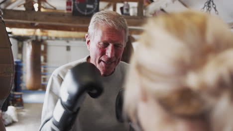 senior male boxer with younger female coach in gym using training gloves