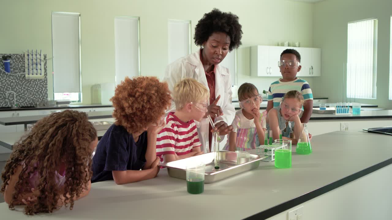 Scienziata in camice da laboratorio che insegna a sei bambini, mostra una provetta e trasferisce del liquido verde su un bancone da laboratorio