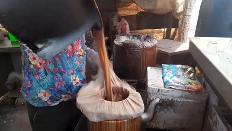 the tea seller is straining the tea with a cloth and pouring it into the kettle