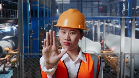 close up of asian female engineer with safety helmet disapproving with no hand sign while standing in factory manufacture of wind turbines