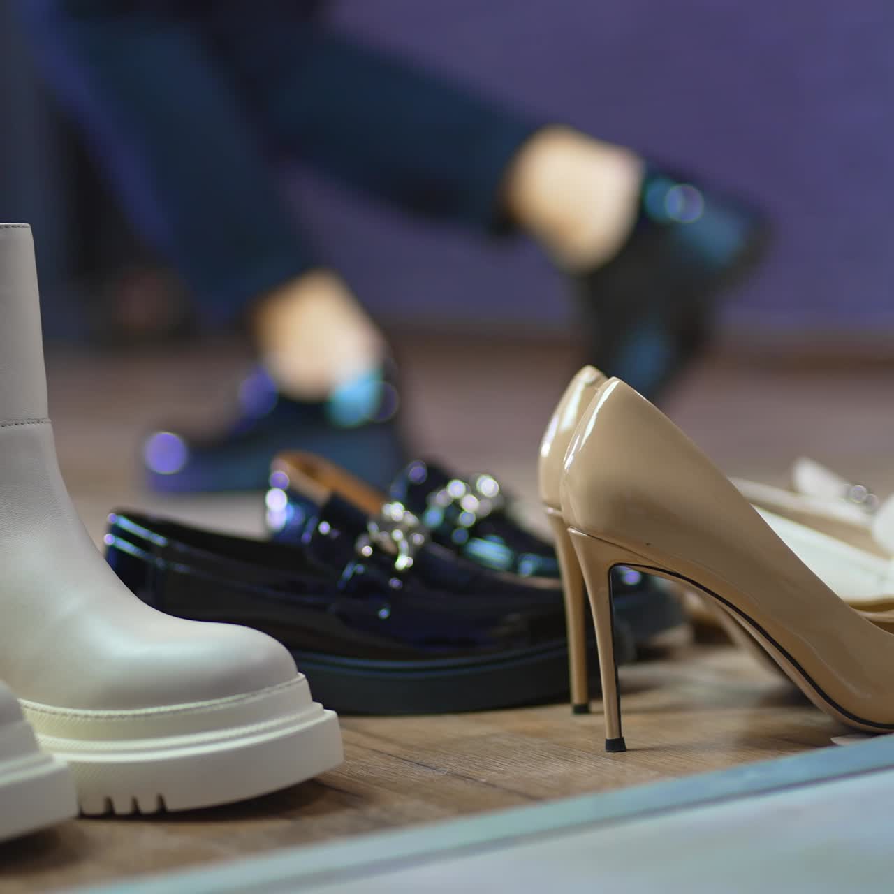 Diverse kinds of female shoes on the floor at foreground. Woman in black jeans and shoes jumping at backdrop in blur