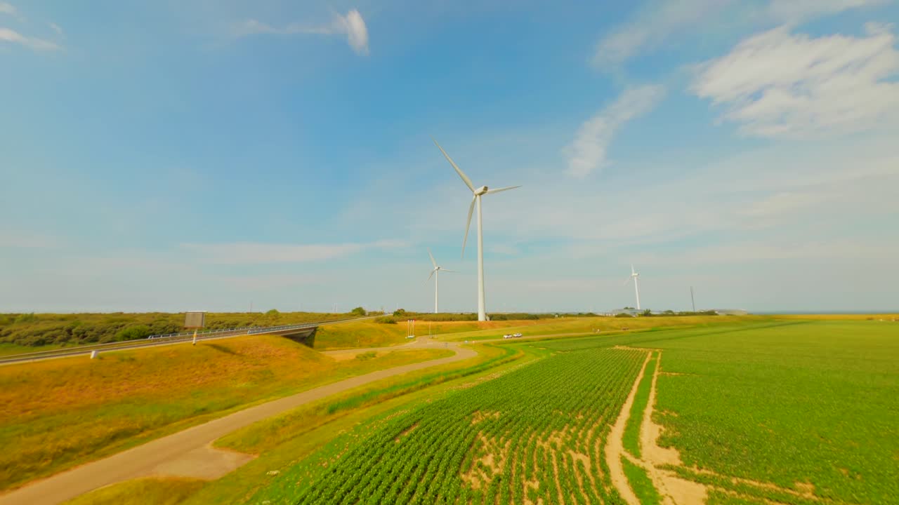 Aerial drone flight over lush green potato field towards modern wind turbine