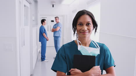 cirujana vestida con exfoliantes y máscara en un concurrido corredor del hospital con colegas en el fondo