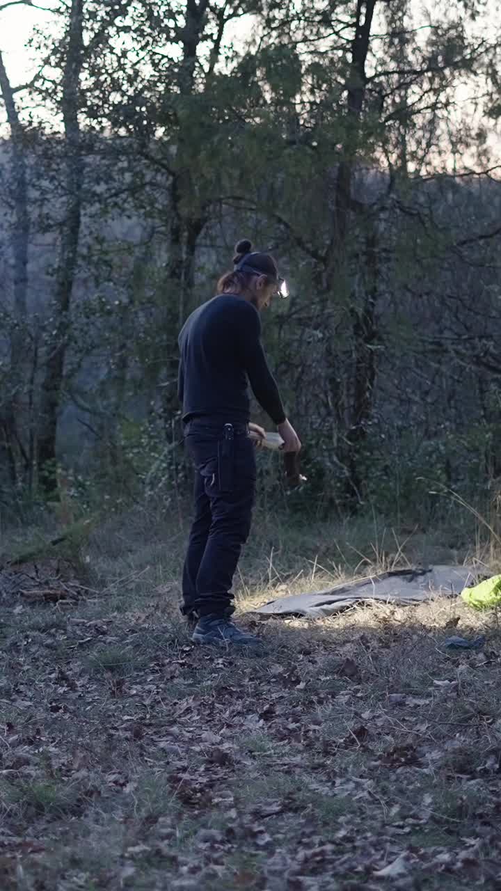 Man camping in the forest at twilight with a headlamp