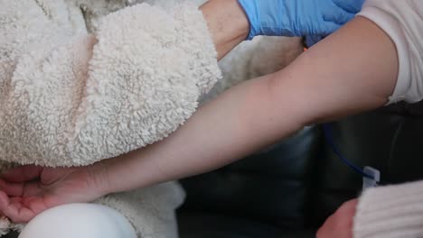 a nurse applies a tourniquet to a patient's arm during a home visit before taking a blood sample