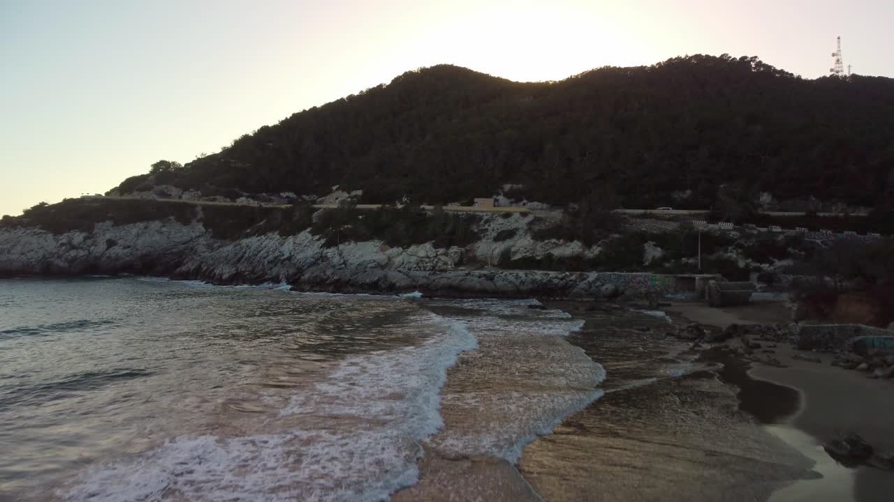 Ora d'oro su una spiaggia serena con onde dolci vicino a una collina rocciosa a Costa Garraf, Spagna