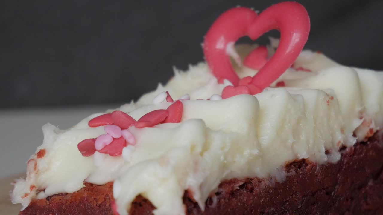 Close-up of a red velvet brownie with white frosting and heart-shaped decoration