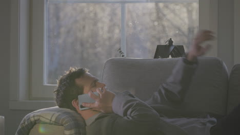 Man-working-on-couch-by-talking-on-phone-and-checking-watch,-side-view