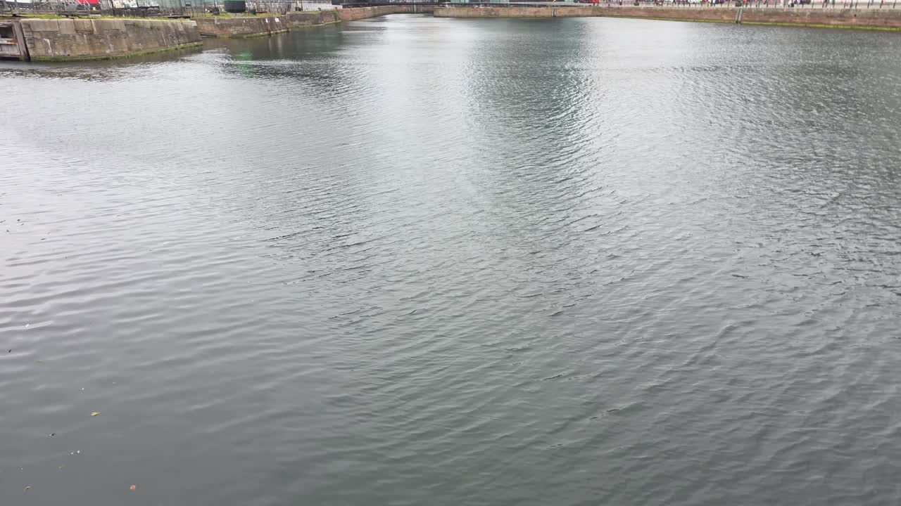 Liverpool, UK — slow tilt-up from dock water to the modern waterfront skyline. Glass towers and historic facades by the Mersey under overcast light