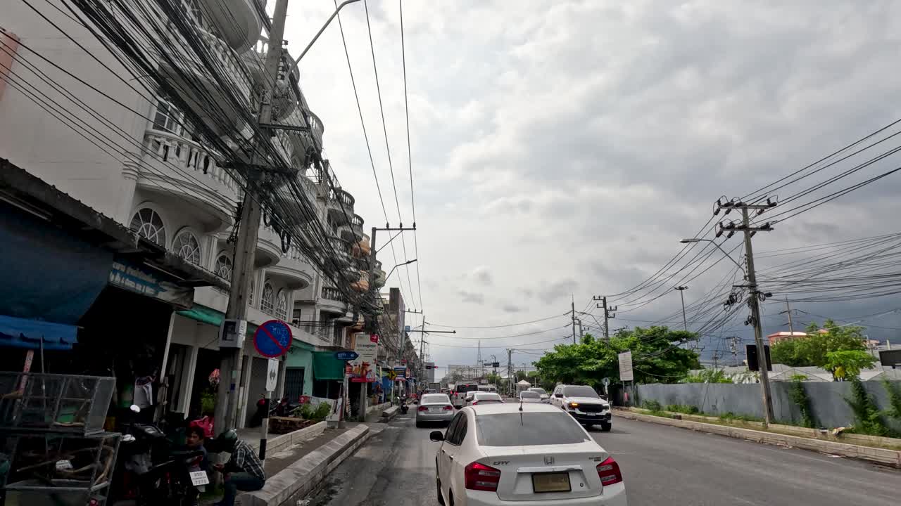 Daytime car journey along a bustling Bangkok street, overcast sky, steady camera, urban environment