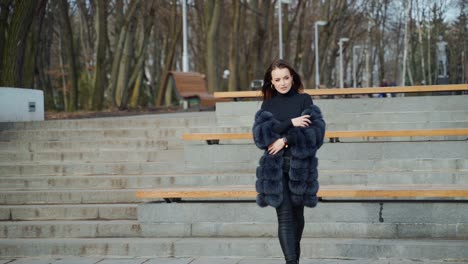 beautiful model posing on camera in autumn park. young woman in black fur coat walking and looking at camera. slow motion.