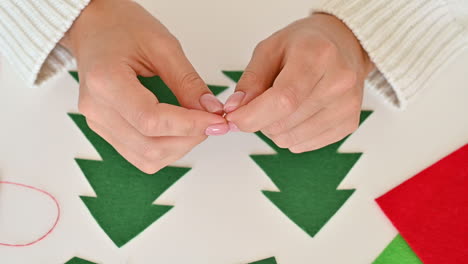 manos femeninas cosen dos árboles de navidad cortados de tela verde