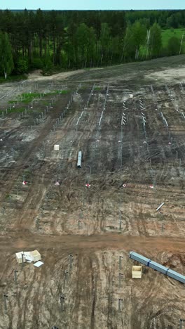 solar farm construction site in latvia with land clearing and mounting posts for solar panels installation - aerial drone vertical shot