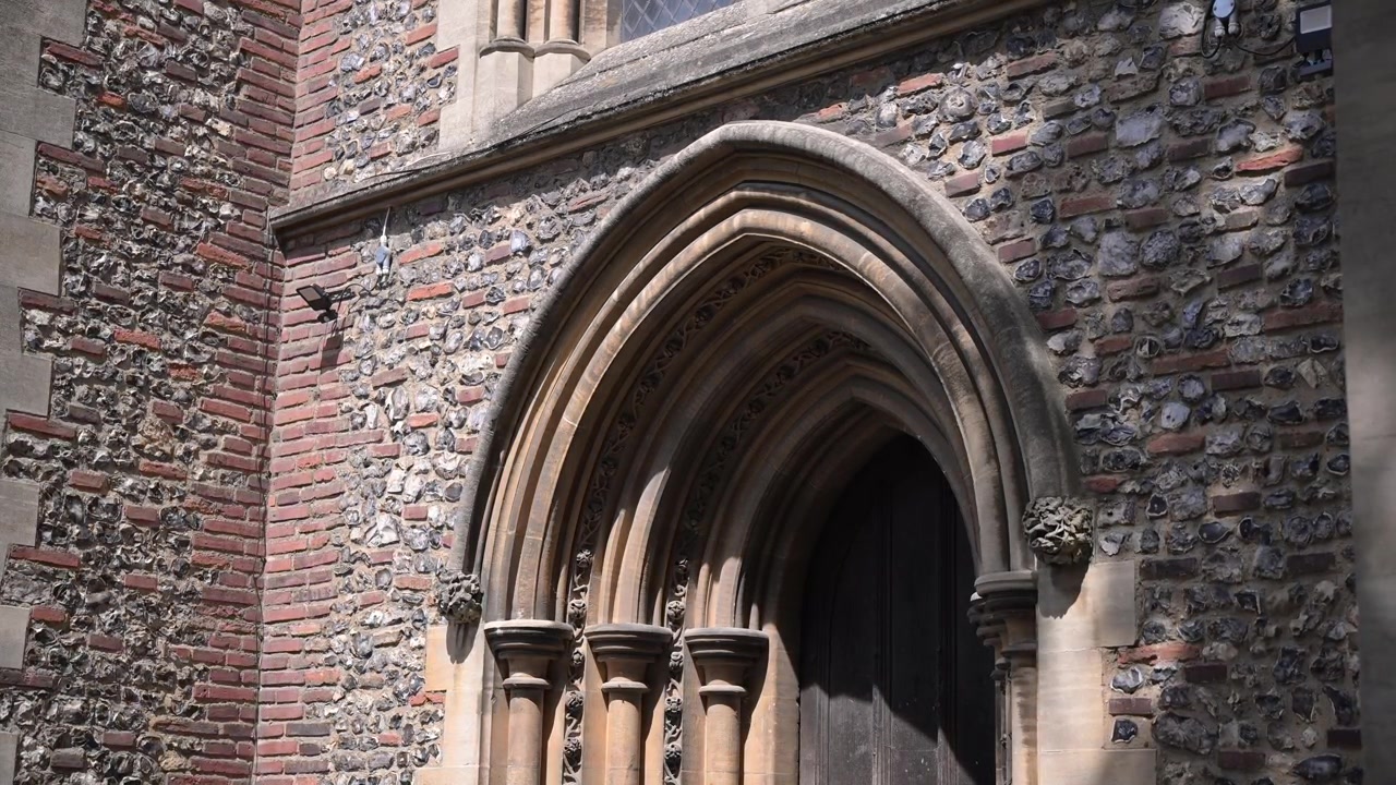 L'ingresso laterale gotico illuminato dal sole della Cattedrale di St Albans rivela dettagliati archi in pietra e muratura in selce in un lento movimento verso l'alto.
