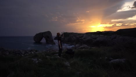 Hiking-man-at-unique-sunrise-ocen-rock-formation-drinking-water-bottle