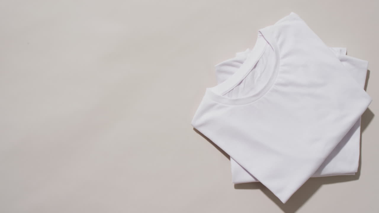 Video of stack of folded white t shirts with copy space on white background