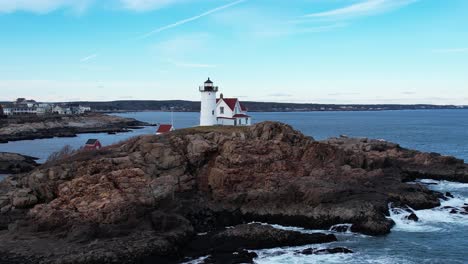 Steady-orbit-of-lighthouse-on-a-rocky-coastal-island-with-tides-crashing-and-blue-sky-above