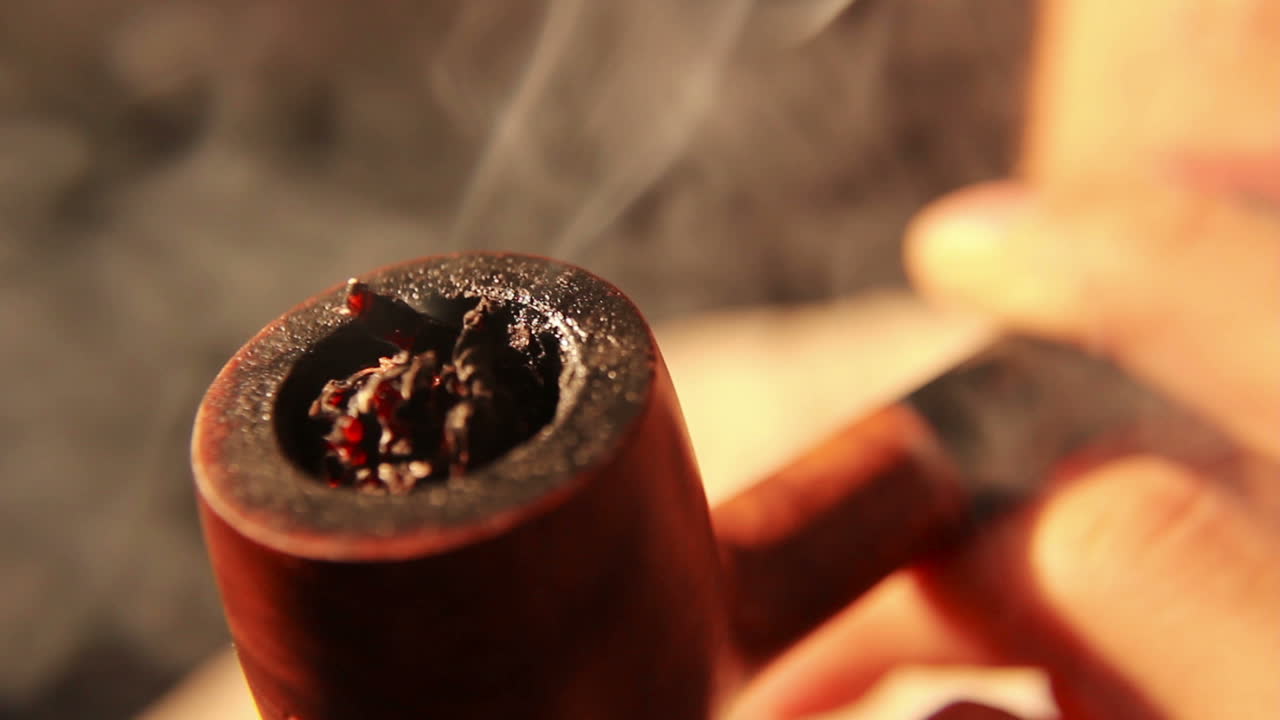 Primo piano di una persona che accende e fuma una pipa di tabacco.
