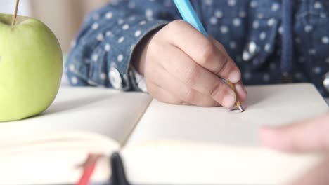 child writing in a notebook with an apple nearby