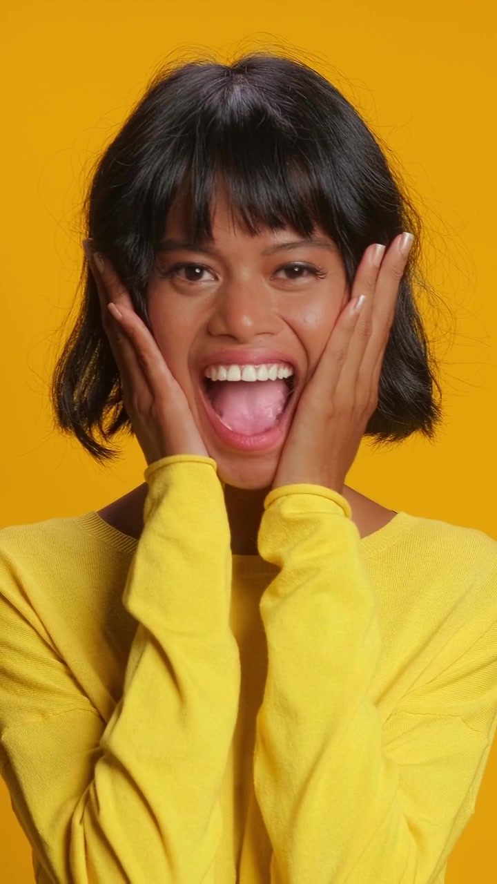 Touched southeast asian woman gasping and holding hands on chest over yellow