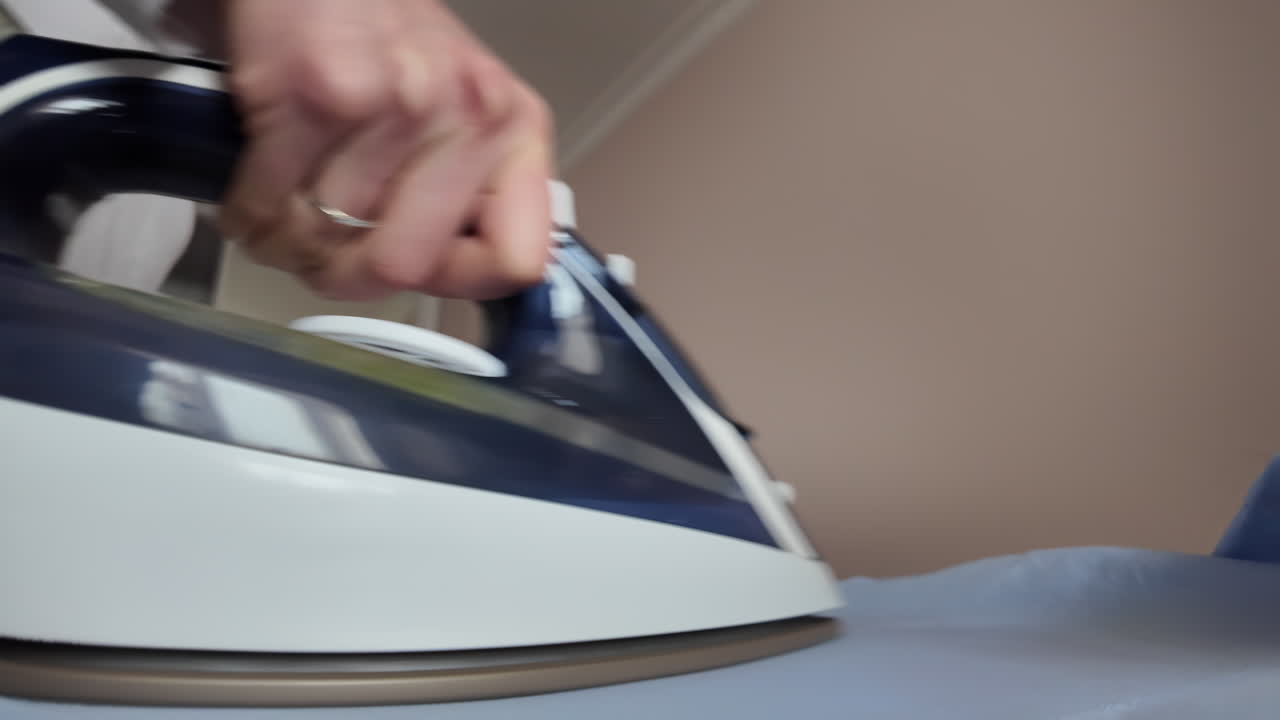 Close up woman ironing a blue shirt at home with white steam