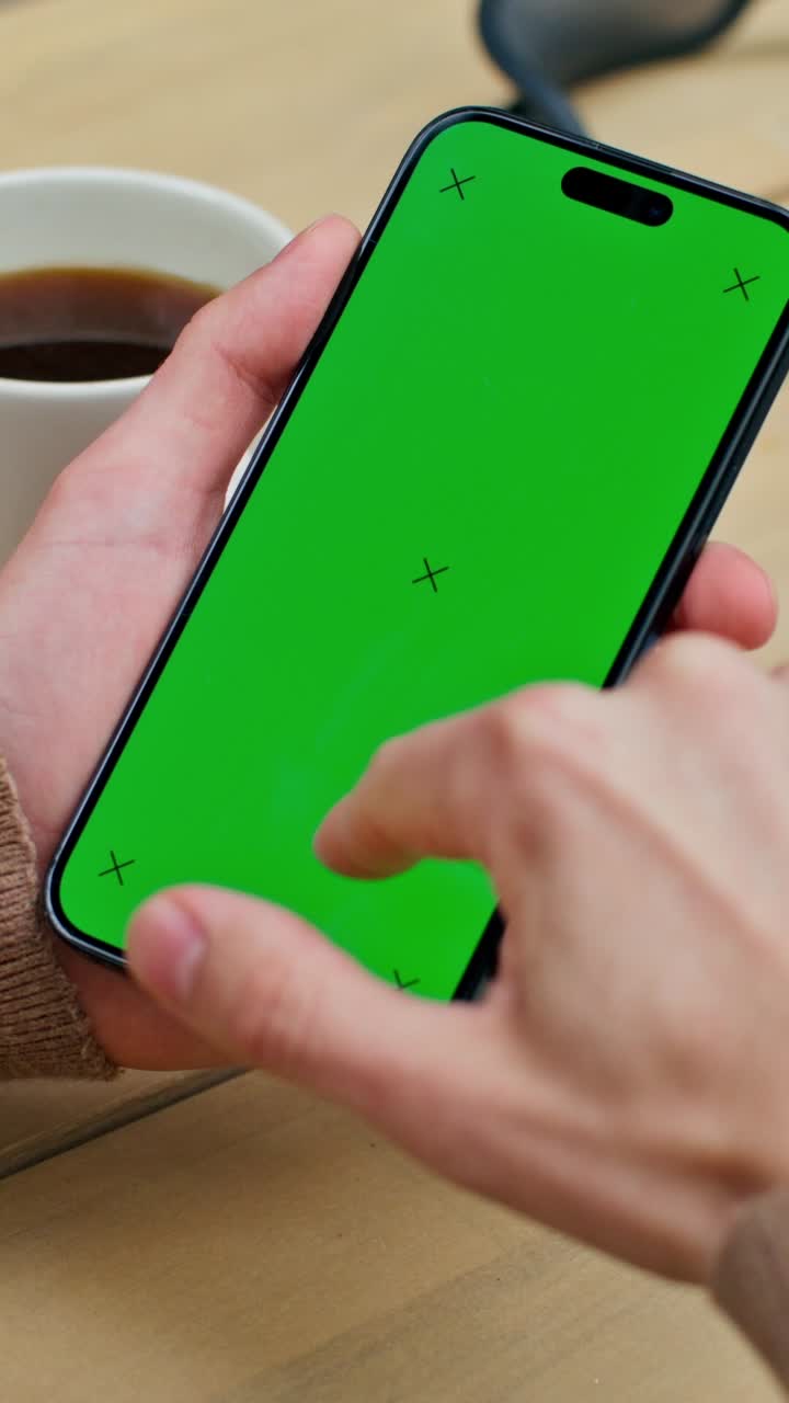 persona usando un teléfono inteligente con una pantalla verde, taza de café en la mesa