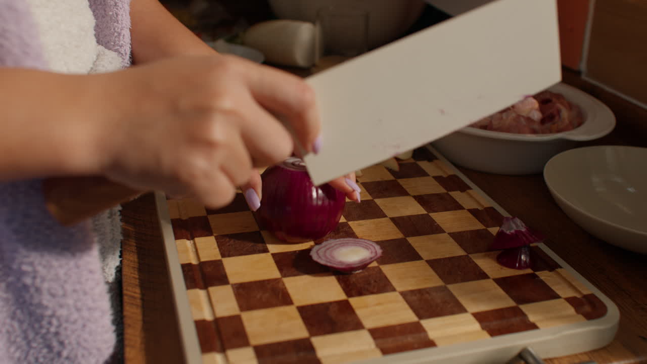 Person chopping onion on wooden board, preparing dinner in cozy kitchen