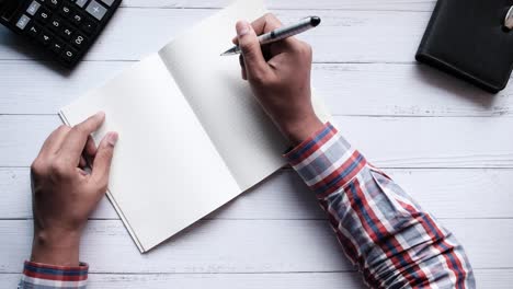 persoon die in een notitieboek op een bureau schrijft