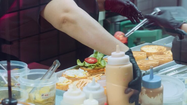 Filmato cinematografico 4K di cucina di uno chef che prepara e realizza un delizioso hamburger fatto in casa nella cucina di un ristorante al rallentatore, mettendo i diversi condimenti e gli hamburger sui panini