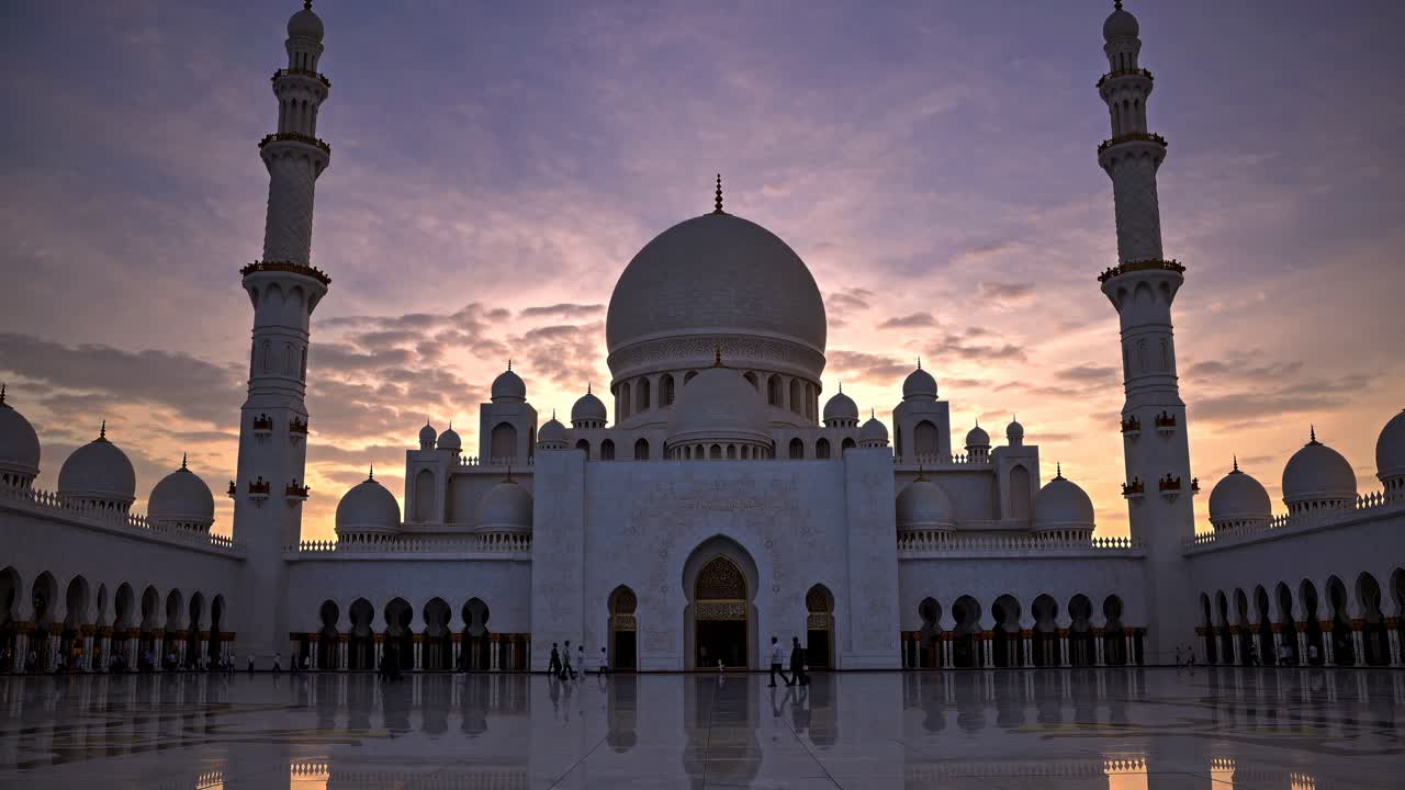 Video con angolazione dal basso di una grande moschea al tramonto, che mostra le sue cupole e i minareti in silhouette