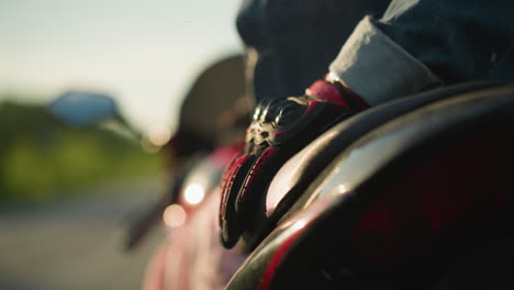 disparo en primer plano de la mano con guante de un motociclista descansando en el asiento de una bicicleta eléctrica roja, con un borrón suave en el fondo