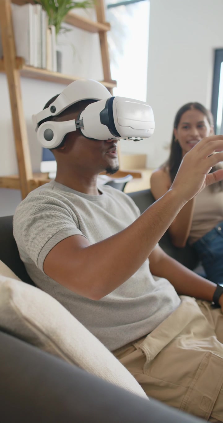 Video verticale: Coppia sul divano che guarda un uomo con un visore VR esplorare l'interfaccia utente, mentre la donna ha un tablet.