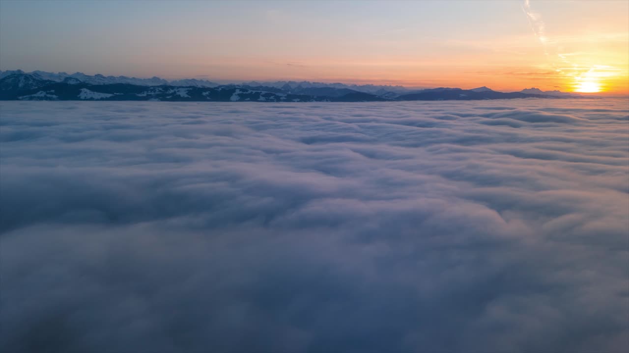 Drone flight at sunset over a sea of fog. Aerial view in the Swiss Alps. The mountain ranges are visible in the background. It is winter. Hyperlapse in a beautiful natural landscape
