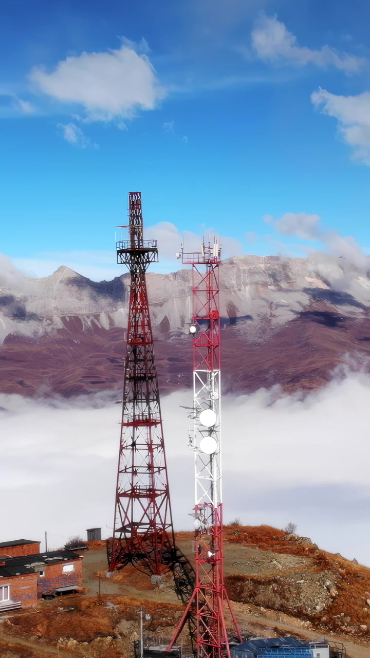 Complesso di torri di telecomunicazione sopra le nuvole, ampia vista aerea di torri a traliccio rosse accanto a edifici di manutenzione, mare.