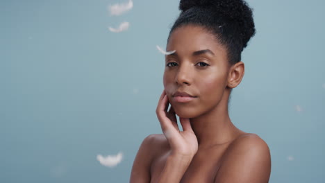 slow motion beauty portrait attractive african american woman feathers falling on smooth skin touching bare shoulders enjoying natural skincare gently caressing body in blue background
