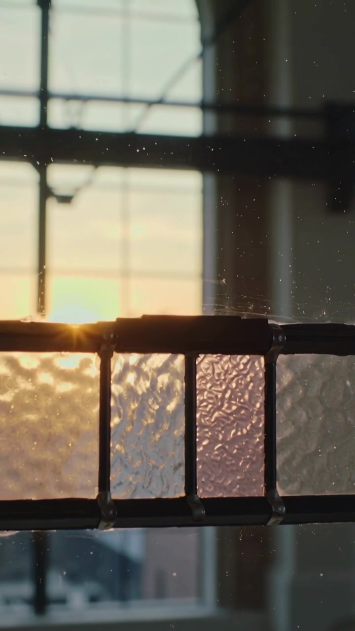 Vertical video: Shifting low sun lighting textured leaded-glass band in loft, showing dust