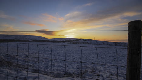 timelapse of a snowy field with a sunset and a open link sheep fence