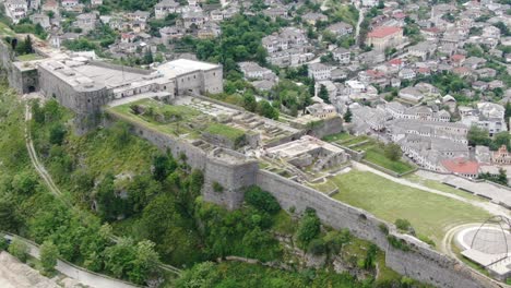 Drone-view-in-Albania-flying-in-Gjirokaster-town-over-a-medieval-castle-on-high-ground-fort-showing-the-brick-brown-roof-houses