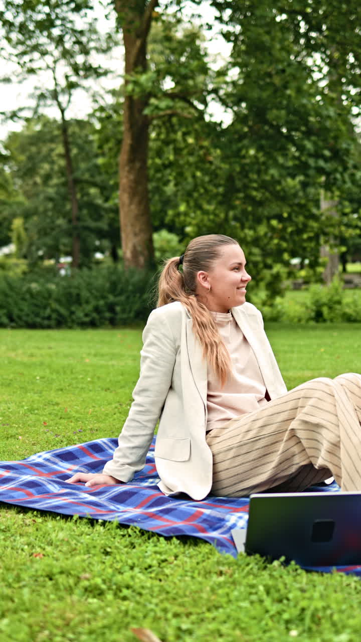 En selvsikker kvinde studerer og arbejder eksternt på sin bærbare computer, mens hun sidder på græsset i en bypark. Hun kombinerer arbejde på afstand med fritid. Ensom forretningskvinde arbejder på sin bærbare computer i parken.
