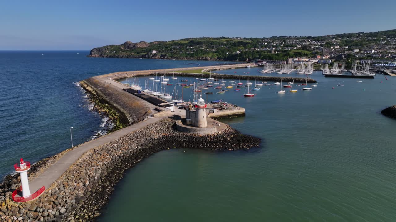 Howth Harbour, County Dublin, Ireland, May 2023. Drone orbits counter clockwise around the Lighthouse at the mouth of the harbour on a bright sunny afternoon with Ireland's Eye in the background.
