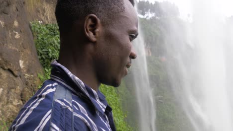 close up shot of an african mans face as he stands behind a pouring waterfall