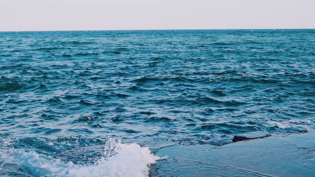 Waves crashing on stone beach. Amazing view of sea water. Blue water surface. Beautiful motion of sea water. Slow motion.