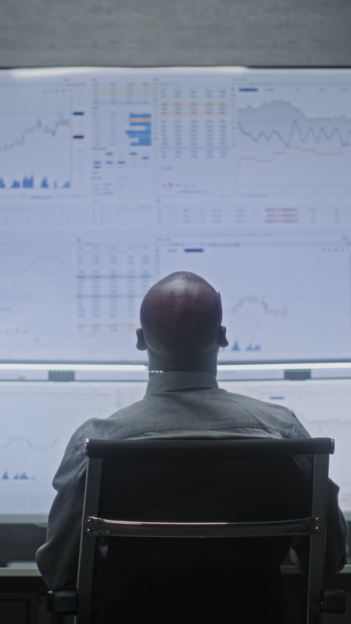 Financial Analyst Working on Computer with Multi-Monitor Workstation, Monitoring Real-Time Stocks and Exchange Market Charts. African American Businessman Works in Bank Office at Night. Vertical Shot.