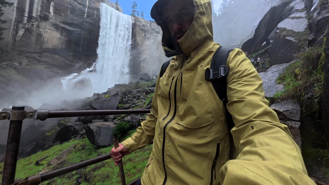 Yosemite'de coşkulu bir şelalenin yanında duran yağmurluklu adam