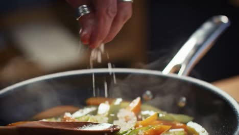 professional chef carefully seasoning sizzling vegetables in a hot skillet
