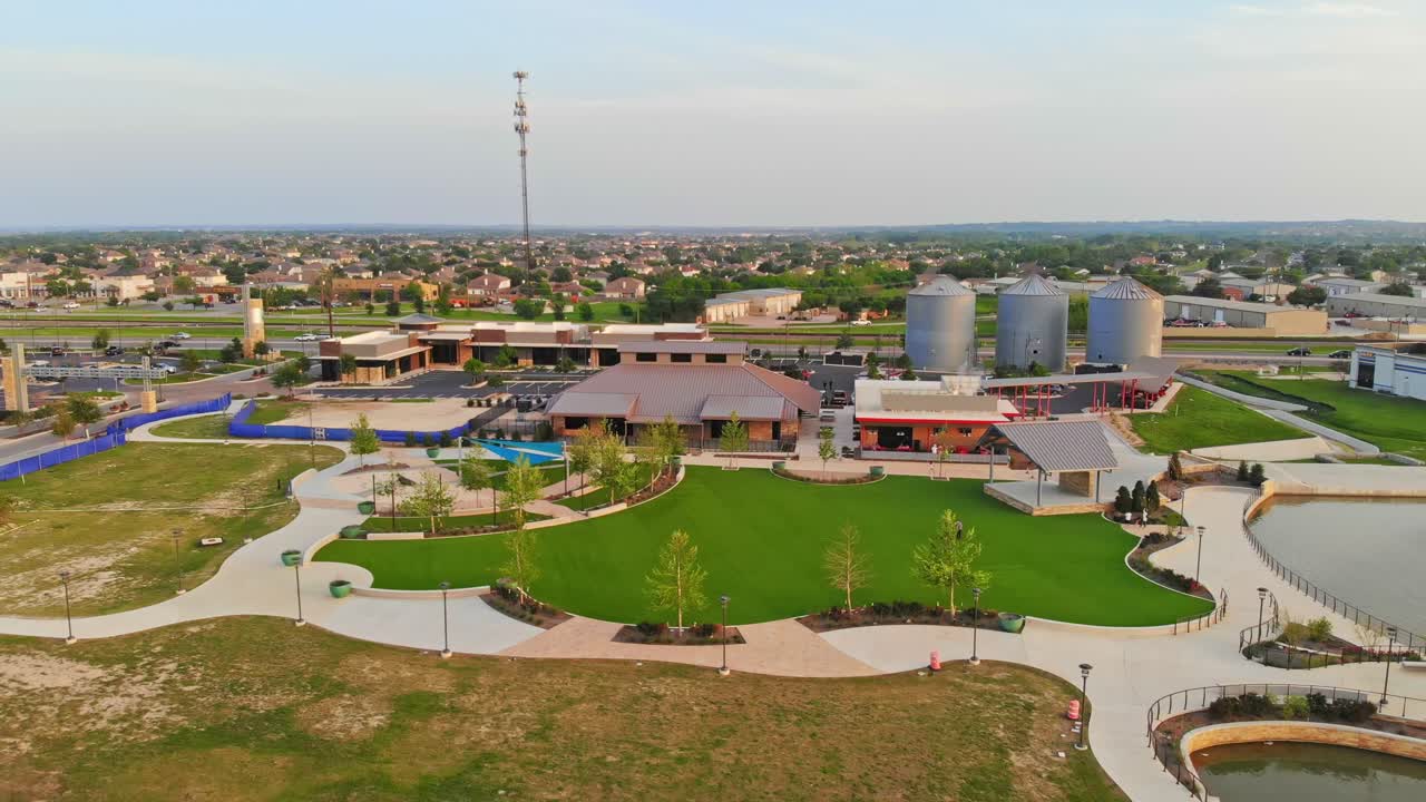 espacio de restaurante en el centro de la ciudad detrás de los silos icónicos que bordean la carretera principal, alejándose de una plataforma de salpicaduras a la izquierda, un gran espacio verde al aire libre en el centro y un pequeño escenario cubierto a la derecha