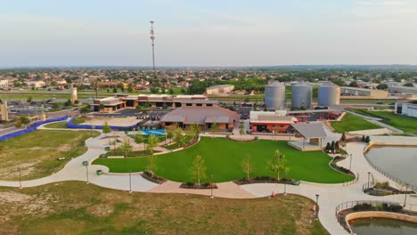 Downtown-restaurant-space-behind-iconic-silos-that-line-the-main-road,-pulling-away-from-a-splash-pad-on-the-left,-a-large-outdoor-greenspace-in-the-center,-and-a-small-covered-stage-on-the-right